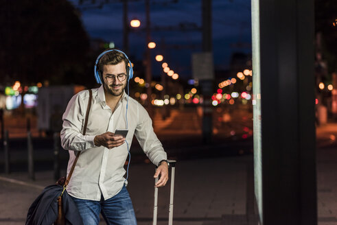 Junger Mann in der Stadt mit Kopfhörern und Mobiltelefon bei Nacht - UUF10869