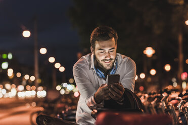 Young man in the city checking cell phone at night - UUF10873