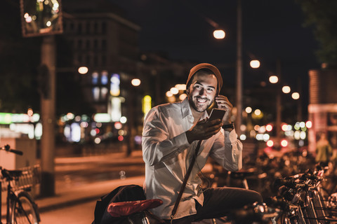 Junger Mann in der Stadt mit Ohrhörern und Mobiltelefon bei Nacht, lizenzfreies Stockfoto