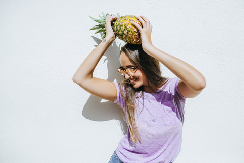 Glückliche junge Frau hält Ananas vor einer weißen Wand, lizenzfreies Stockfoto
