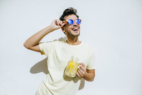 Young an with sunglasses and lemonade in front white wall - KIJF01516
