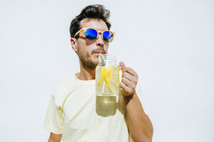 Mann mit Sonnenbrille trinkt Limonade vor weißer Wand - KIJF01517