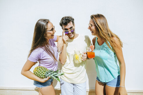 Glückliche Freunde halten erfrischende Getränke und Ananas vor einer weißen Wand - KIJF01519