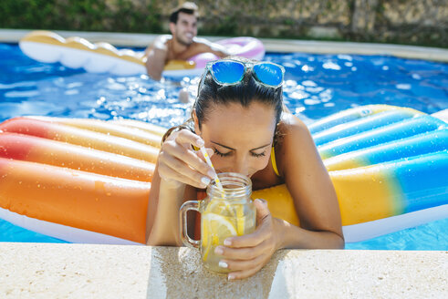 Junge Frau im Schwimmbad mit Getränk am Beckenrand - KIJF01532