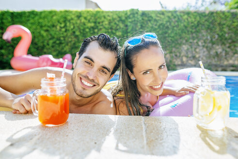 Happy couple in swimming pool with drinks at the poolside - KIJF01534