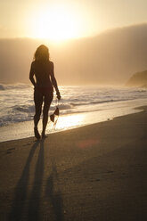 Mexiko, Riviera Nayarit, Silhouette einer Frau, die am Strand in den Sonnenuntergang läuft und dabei ihr Bikinioberteil festhält - ABAF02164