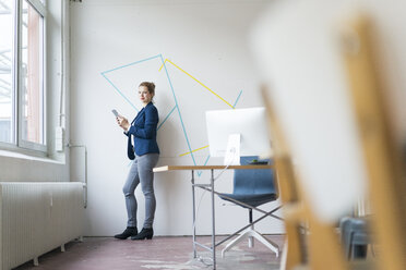 Businesswoman standing in office using digital tablet - JOSF01133