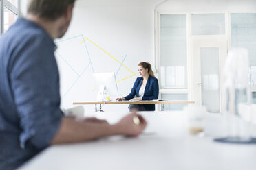 Geschäftsfrau bei der Arbeit im Büro mit einem im Vordergrund sitzenden Kollegen - JOSF01146