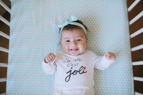 Glückliches Baby mit einem Haarband in der Krippe liegend, lizenzfreies Stockfoto