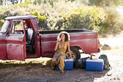 Junge Frau sitzt neben einem alten rostigen Pick-up-Truck und trinkt aus einer Flasche - ZEF13892