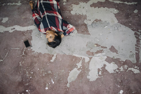 Woman lying on cracked floor with cell phone - KNSF01518