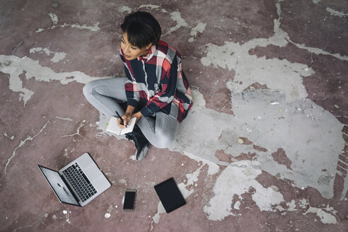 Woman sitting on cracked floor with notebook - KNSF01528