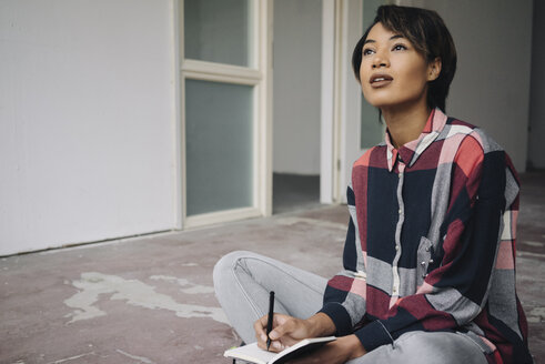 Woman sitting on cracked floor with notebook - KNSF01530