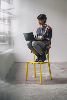 Young woman sitting on chair using laptop - KNSF01532