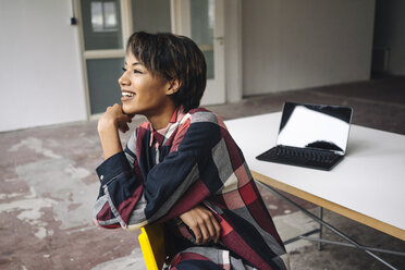 Smiling woman sitting on chair with laptop on table - KNSF01535