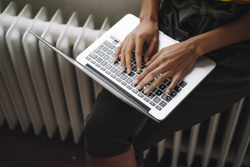 Woman sitting on heater using laptop - KNSF01540