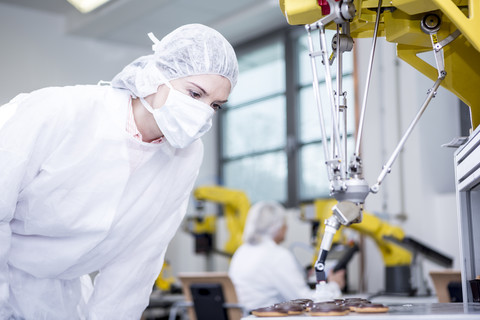 Frau in Fabrik, die einen Roboter bei der Handhabung von Keksen untersucht, lizenzfreies Stockfoto