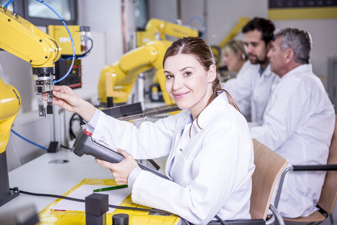 Portrait of smiling engineer examining industrial robot - WESTF23407