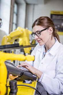 Woman using device in factory with industrial robots - WESTF23414