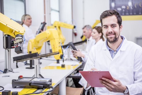 Portrait of smiling engineer in factory with clipboard - WESTF23415