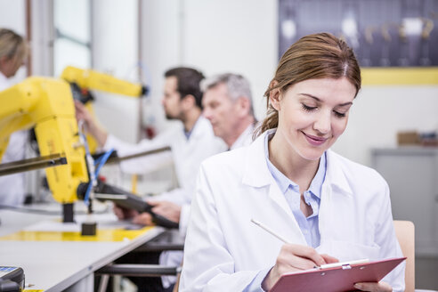 Engineer in factory taking notes on clipboard - WESTF23416