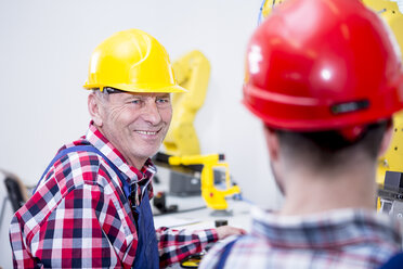 Mann in einer Fabrik mit Schutzhelm lächelt einen Kollegen an - WESTF23424