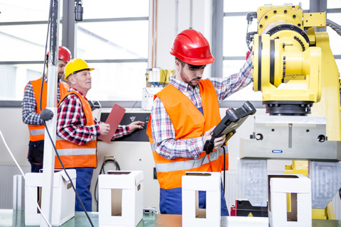 Drei Männer in einer Fabrik mit Industrieroboter, lizenzfreies Stockfoto