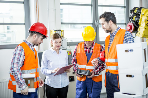 Mitarbeiter besprechen sich in einer Fabrik mit einem Industrieroboter im Hintergrund, lizenzfreies Stockfoto