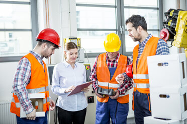 Mitarbeiter besprechen sich in einer Fabrik mit einem Industrieroboter im Hintergrund - WESTF23431