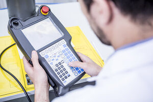 Close-up of man using control for industrial robot - WESTF23432