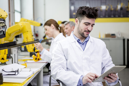 Engineer holding tablet with industrial robots in background - WESTF23435