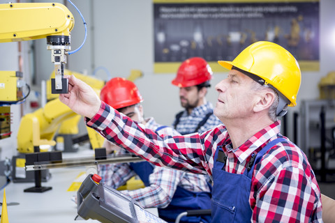 Mann mit Schutzhelm stellt Industrieroboter ein, lizenzfreies Stockfoto