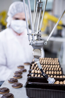 Woman in factory looking at robot handling cookies - WESTF23452