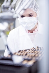 Frau in Fabrik mit Blick auf einen Roboter, der Kekse verarbeitet - WESTF23453