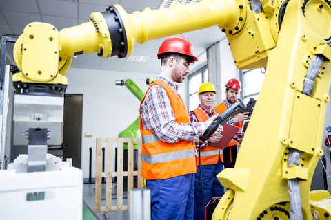 Drei Männer in einer Fabrik mit Industrieroboter, lizenzfreies Stockfoto