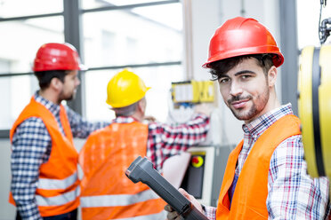 Porträt eines selbstbewussten Mannes mit Schutzhelm in einer Fabrik - WESTF23459