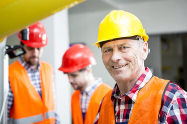 Porträt eines lächelnden Mannes mit Schutzhelm in einer Fabrik - WESTF23462