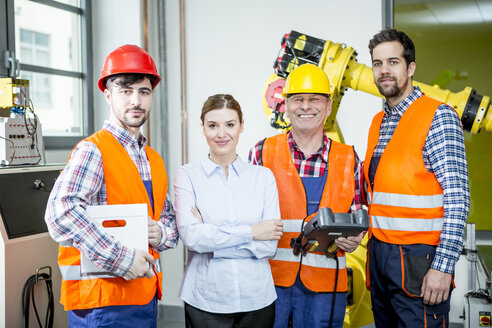 Portrait of confident staff in factory with industrial robot in background - WESTF23465