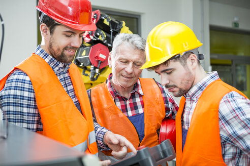 Three men in factory talking with industrial robot in background - WESTF23466