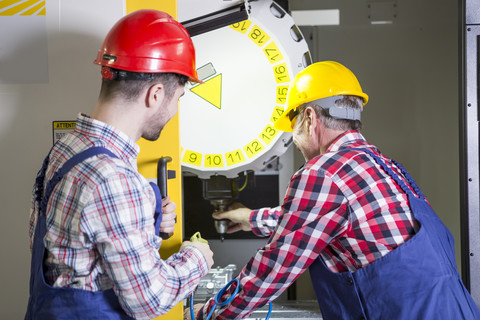 Zwei Männer in einer Fabrik arbeiten an einer CNC-Maschine, lizenzfreies Stockfoto