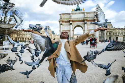 France, Paris, Happy young woman with flying pidgeons at Arc de Triomphe - KIJF01548
