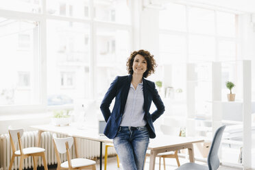 Businesswoman in office sitting on desk, looking confident - KNSF01550