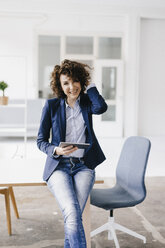 Geschäftsfrau im Büro, auf dem Schreibtisch sitzend, mit digitalem Tablet - KNSF01552