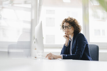 Businesswoman in office sitting at desk - KNSF01564