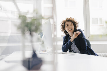 Businesswoman in office sitting at desk, laughing - KNSF01565