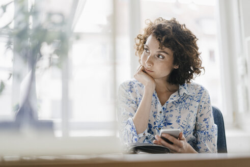 Businesswoman in office with smartphone and diary, looking worried - KNSF01582