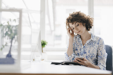 Geschäftsfrau im Büro mit Smartphone und Terminkalender, besorgt dreinblickend - KNSF01583