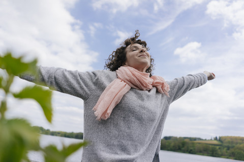 Frau steht am See und tut so, als würde sie fliegen, lizenzfreies Stockfoto