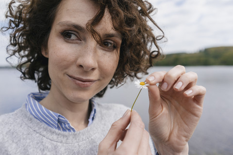 Frau am See zupft Gänseblümchenblüten, lizenzfreies Stockfoto