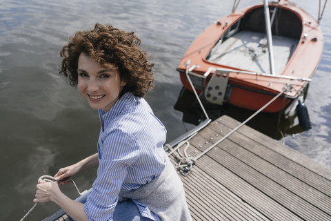 Woman standing on jetty with moored sailing boat stock photo